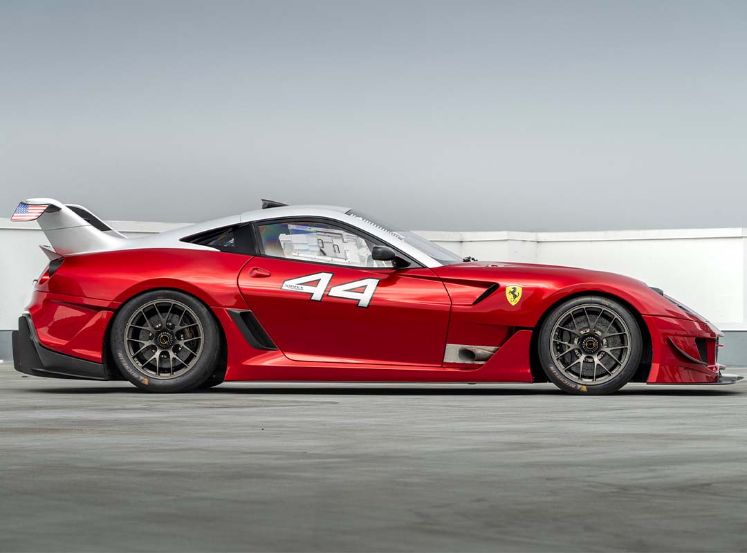Red Ferrari race car with the number 44 and an American flag sticker on the rear, parked on concrete under a clear sky—just the kind of expensive car you'd find at an RM Sotheby's Monterey auction.