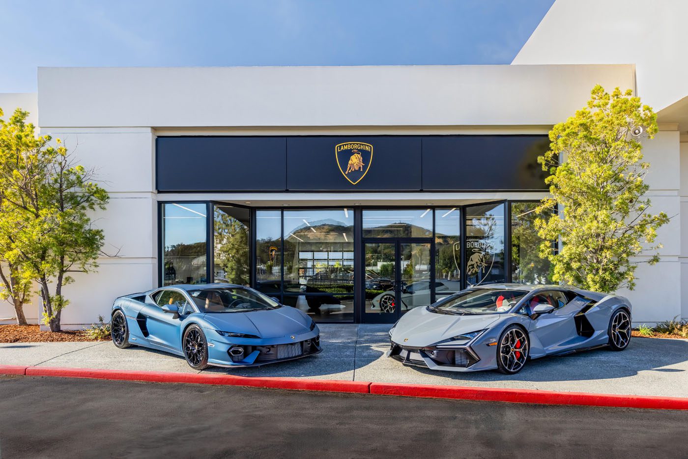 Two silver sports cars are parked in front of a building adorned with the Lamborghini logo. It's a clear sign of an exclusive VIP event at the San Francisco showroom.