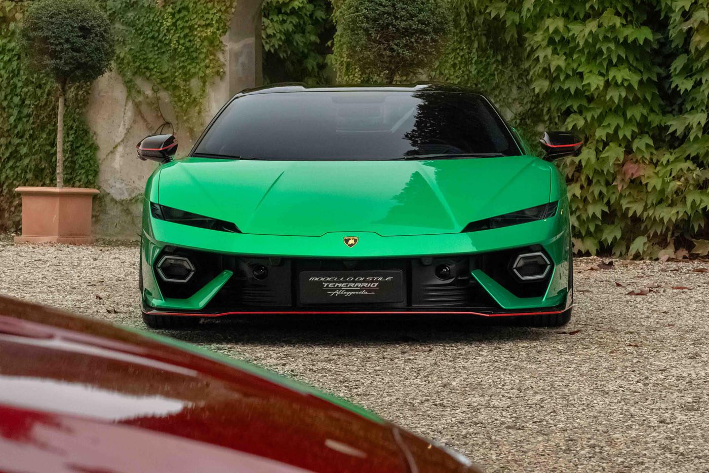 A sleek Lamborghini sports car is parked on a gravel path, surrounded by leafy greenery, embodying the sophisticated design celebrated in the 2024 Autostyle Design Competition in Italy.