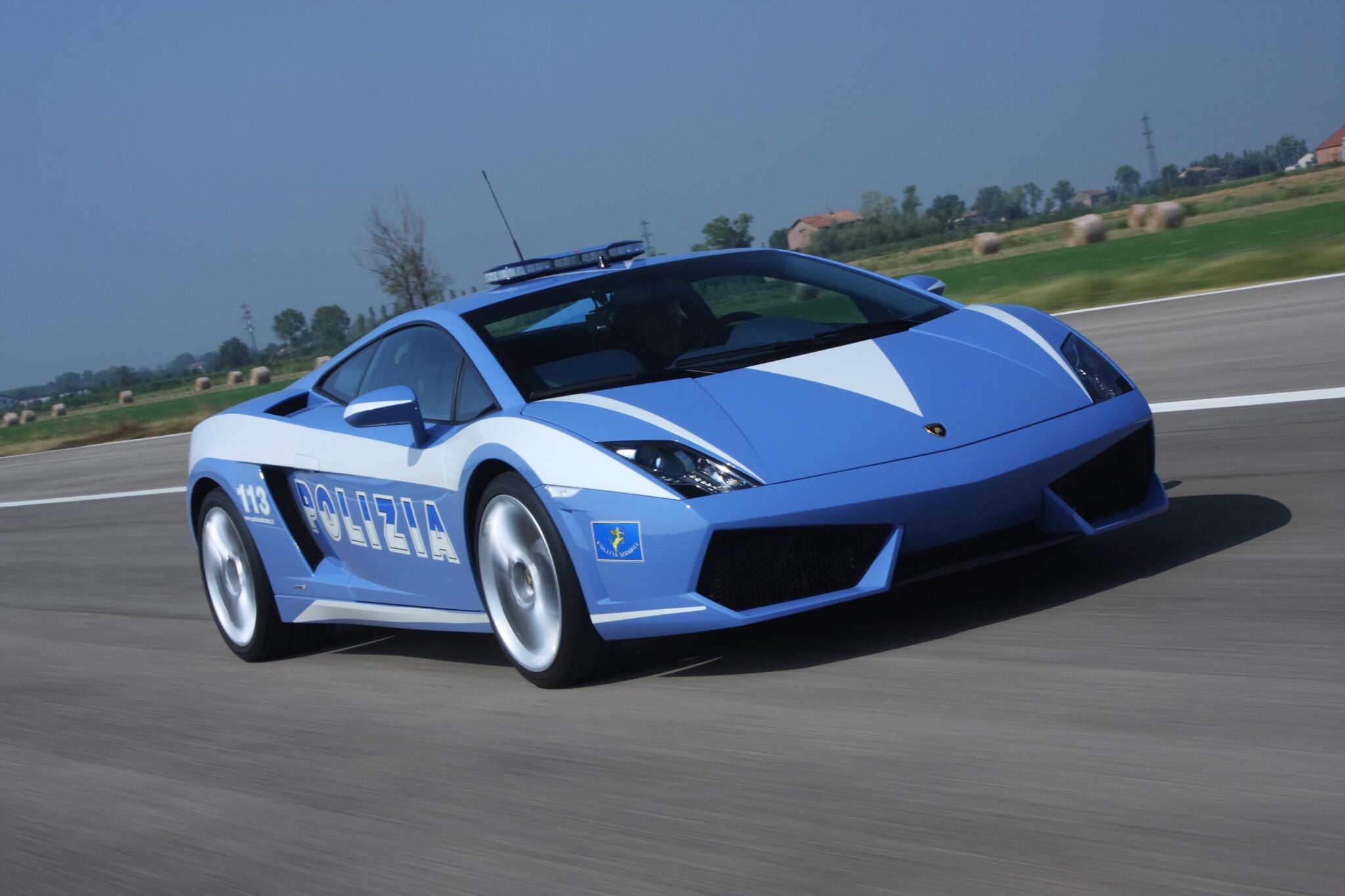 A blue and white Lamborghini of the Italian State Police zips down the road, against a blurred backdrop, highlighting their celebrated 20-year partnership with luxury speed.