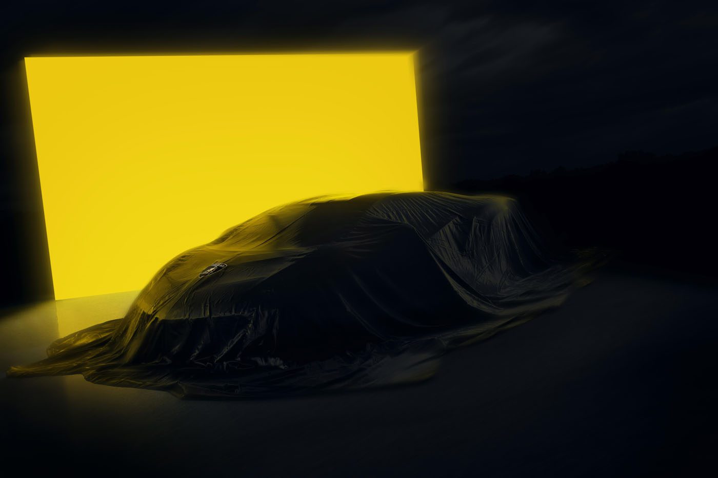 A Lamborghini Few-Off, draped in a dark cloth, stands before a large, bright yellow illuminated rectangle in a dimly lit setting—evoking the exclusive atmosphere of Monterey Car Week.