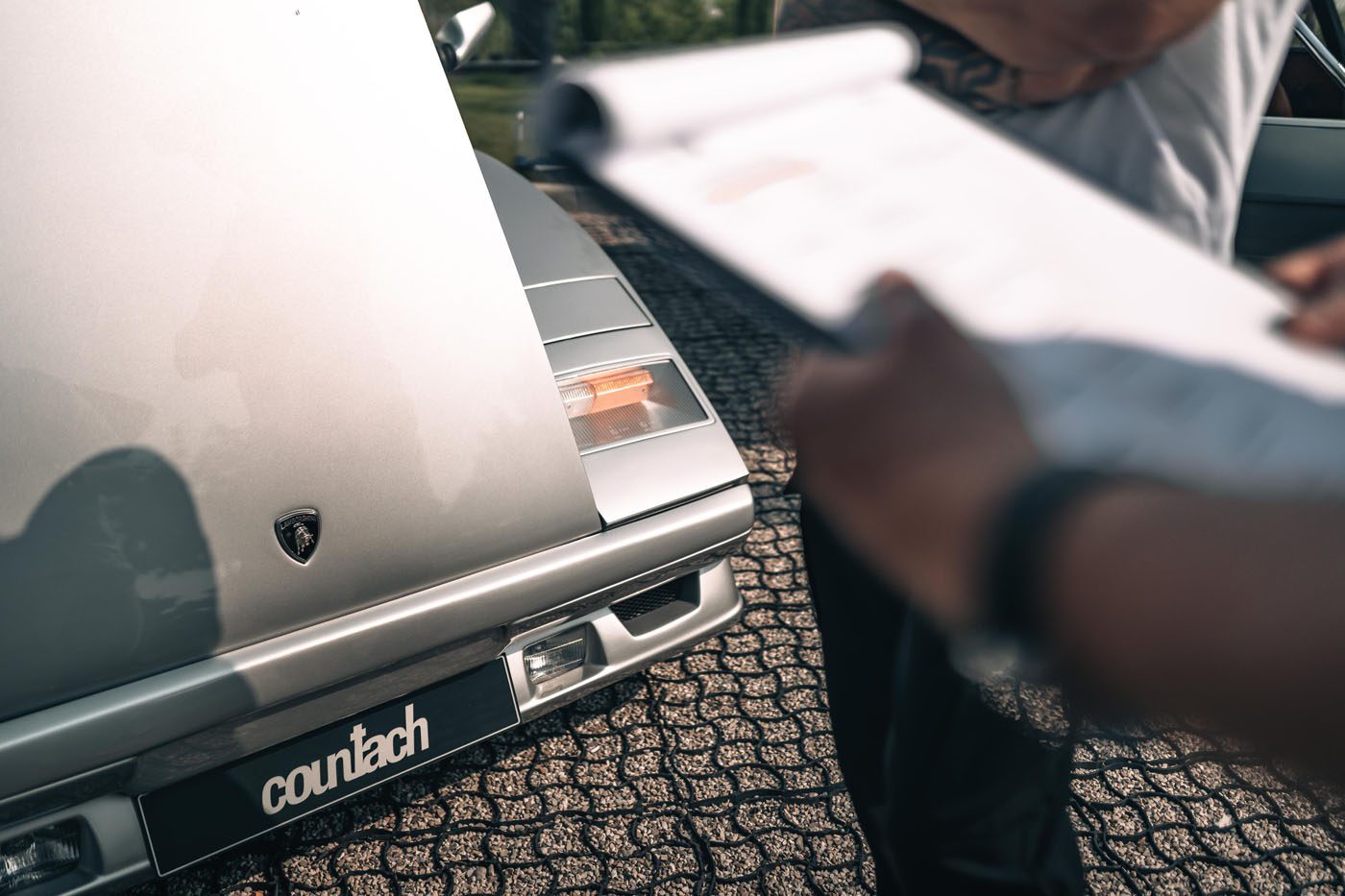 Close-up of a silver Lamborghini Countach with its hood open, while a Polo Storico technician holds a clipboard in the foreground.