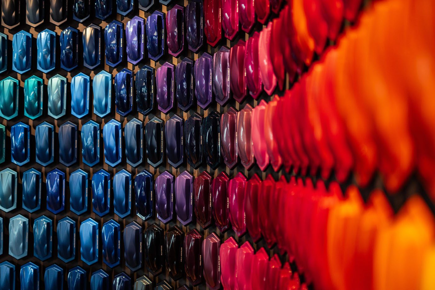 A wall displays an array of car paint samples arranged in hexagonal patterns, featuring a gradient of colors from blue and purple on the left to red and orange on the right—highlighting the origins of iconic Lamborghini colors.