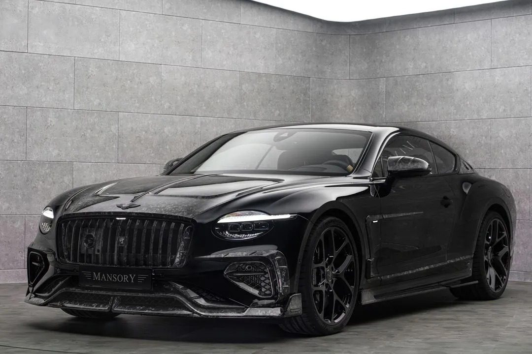 A black Bentley Continental GT with striking Mansory customizations is parked in a modern, gray-tiled showroom with soft, indirect lighting.
