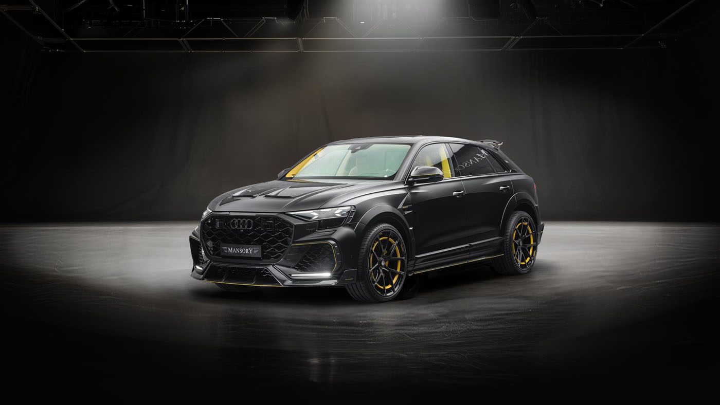 A black Audi SUV with yellow accents is parked on a smooth surface under dramatic studio lighting against a dark background.