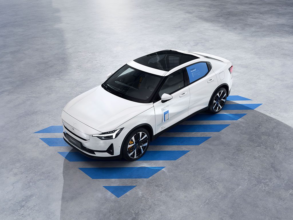 A white electric sedan with a sunroof is parked on a grey surface featuring blue diagonal lines underneath the vehicle.