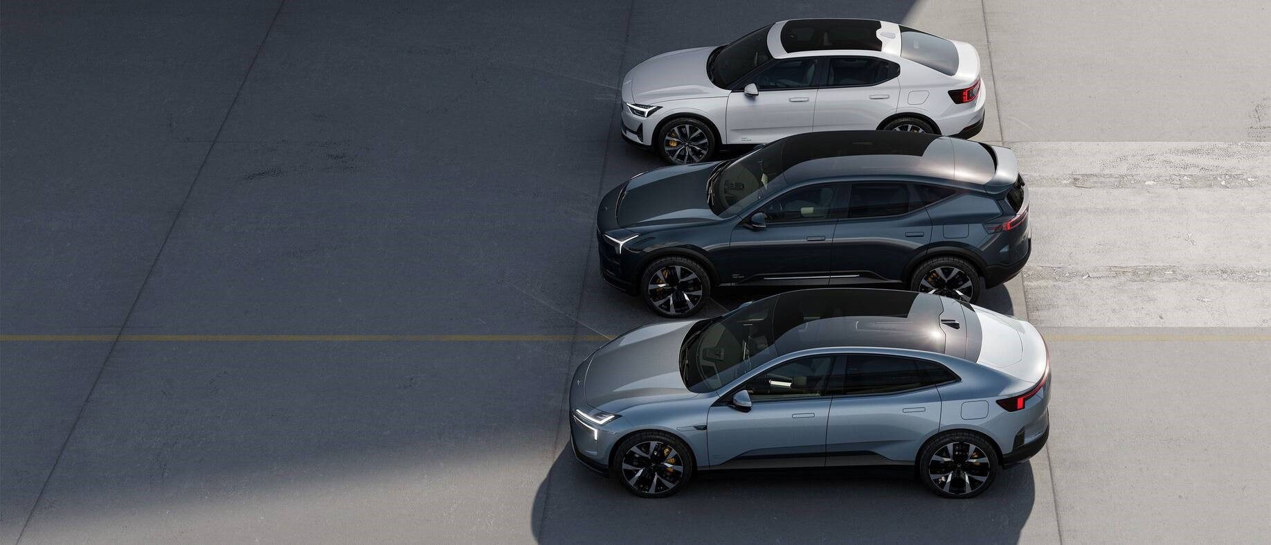 Three modern cars, one white and two grey, are parked in a row on a concrete surface, viewed from above.