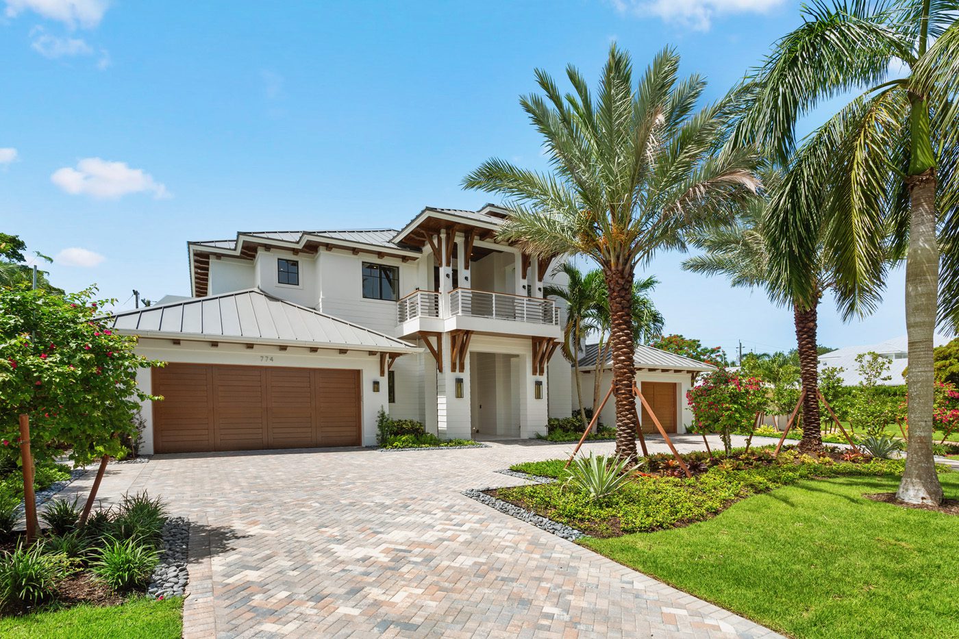 This modern two-story house in Naples features a spacious driveway, palm trees, and a landscaped yard under a clear blue sky, offering a gold standard of high-end real estate.