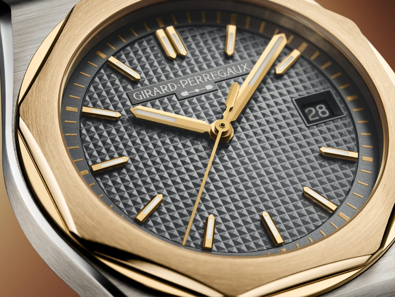 Close-up of a Girard-Perregaux Laureato FIFTY wristwatch featuring a textured black dial, gold hour markers and hands, a date window showing "28," and a gold and steel bezel.
