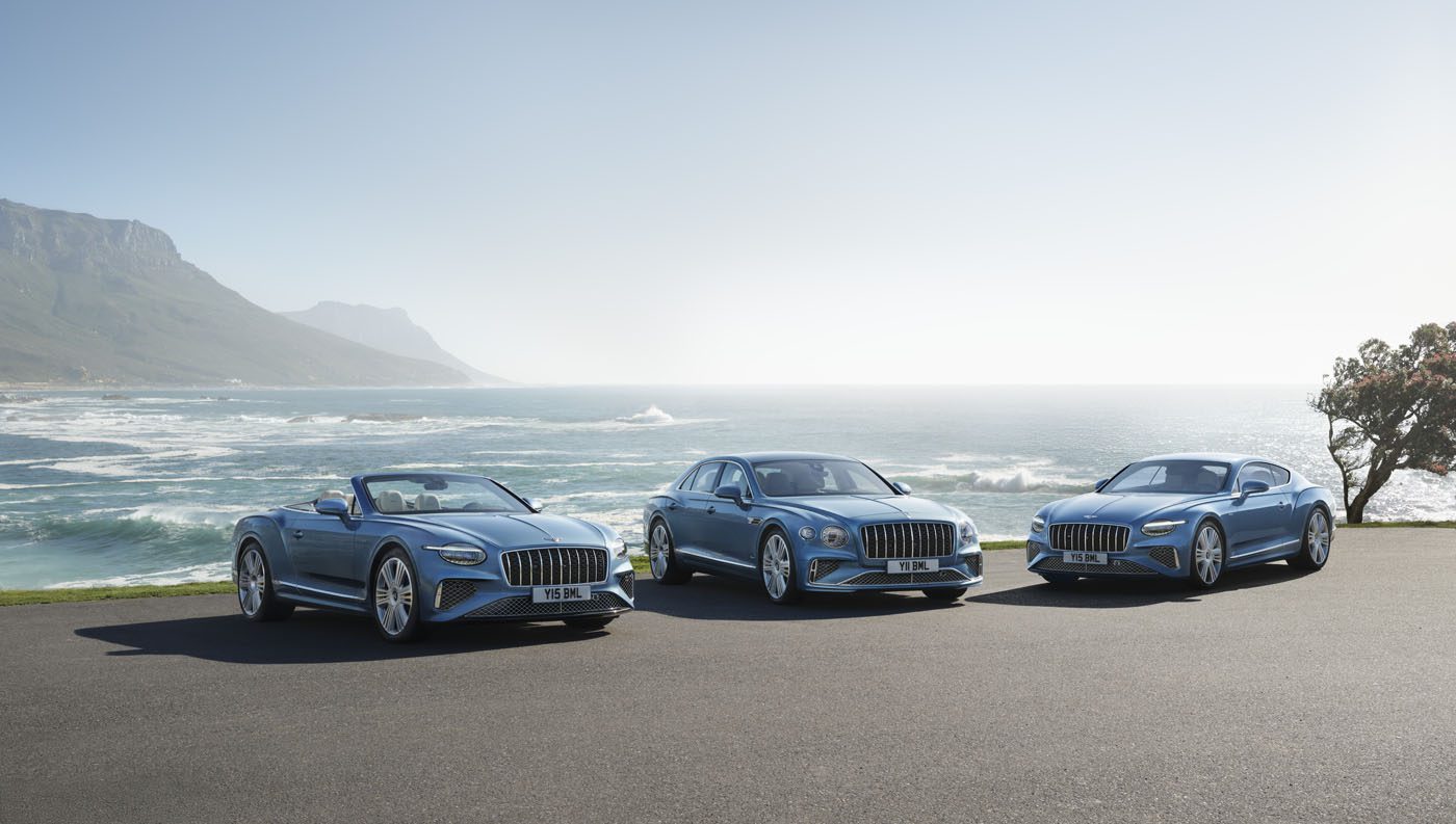 Three blue luxury cars, including a Bentley Continental GT, are elegantly parked on a coastal road. With an ocean backdrop and mountains in the distance, their combined 671HP offers a perfect blend of power and scenic beauty.