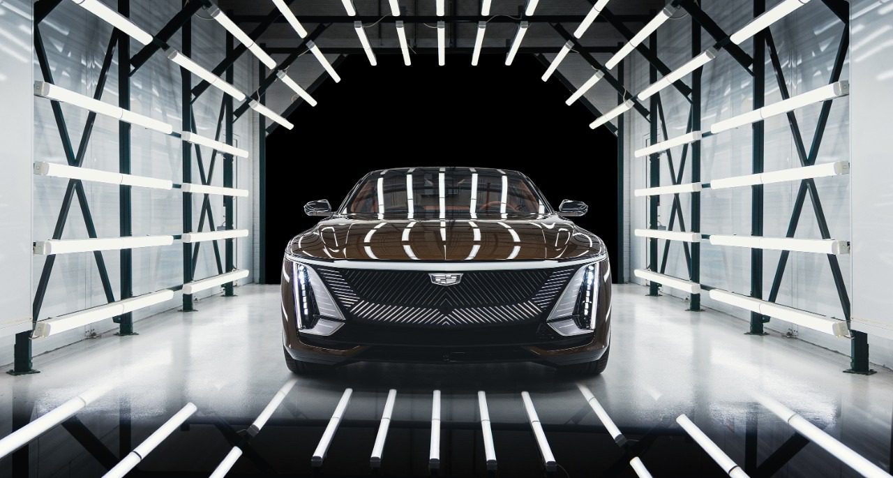 A black Cadillac electric car is positioned under bright, parallel LED lights in a tunnel-like setting, facing the camera directly.