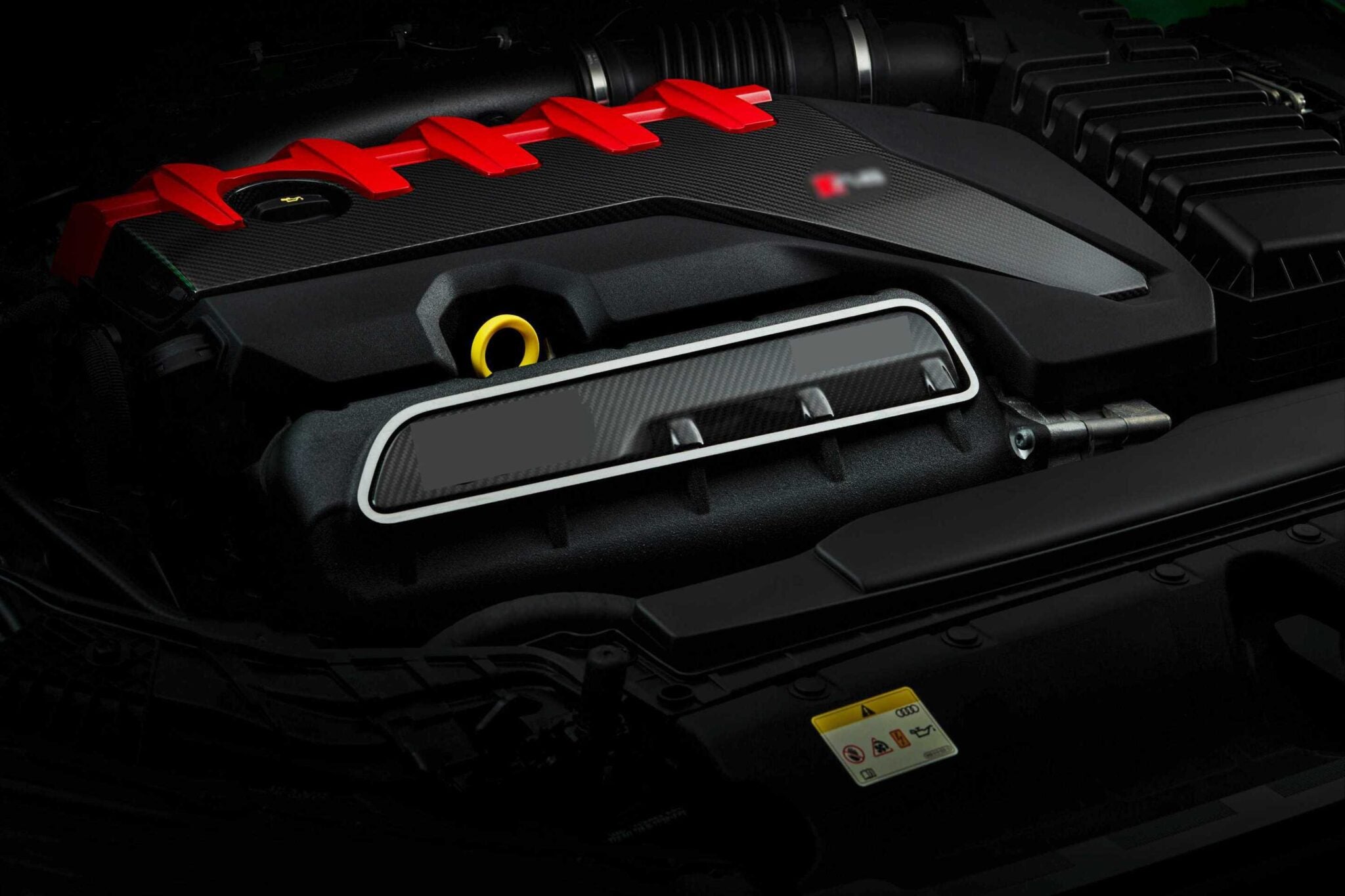 Close-up view of a modern car engine with a red engine cover, black components, and visible warning label—The Last Surviving 5-Cylinder On Sale Today Packs A Punch under the hood.