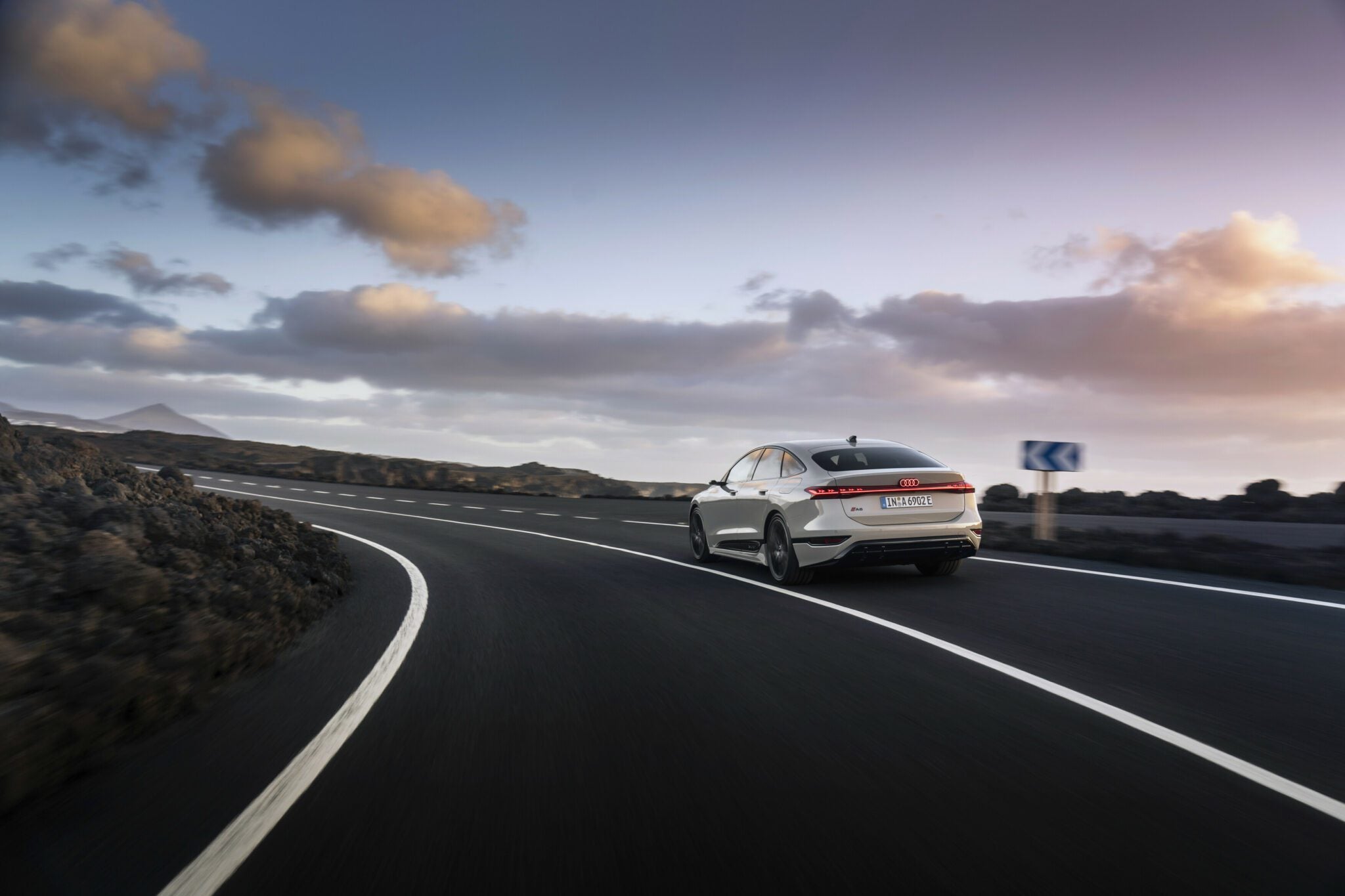 A sleek white car, reminiscent of a Lamborghini, navigates a curving road surrounded by rocky terrain under a partly cloudy sky, symbolizing the Audi Group's anticipated Q3 2024 success.