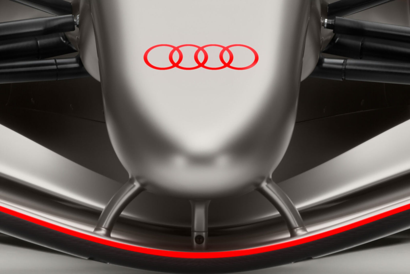 Close-up of the front of an Audi Formula 1 car, featuring the red Audi logo on a silver surface with aerodynamic parts visible.