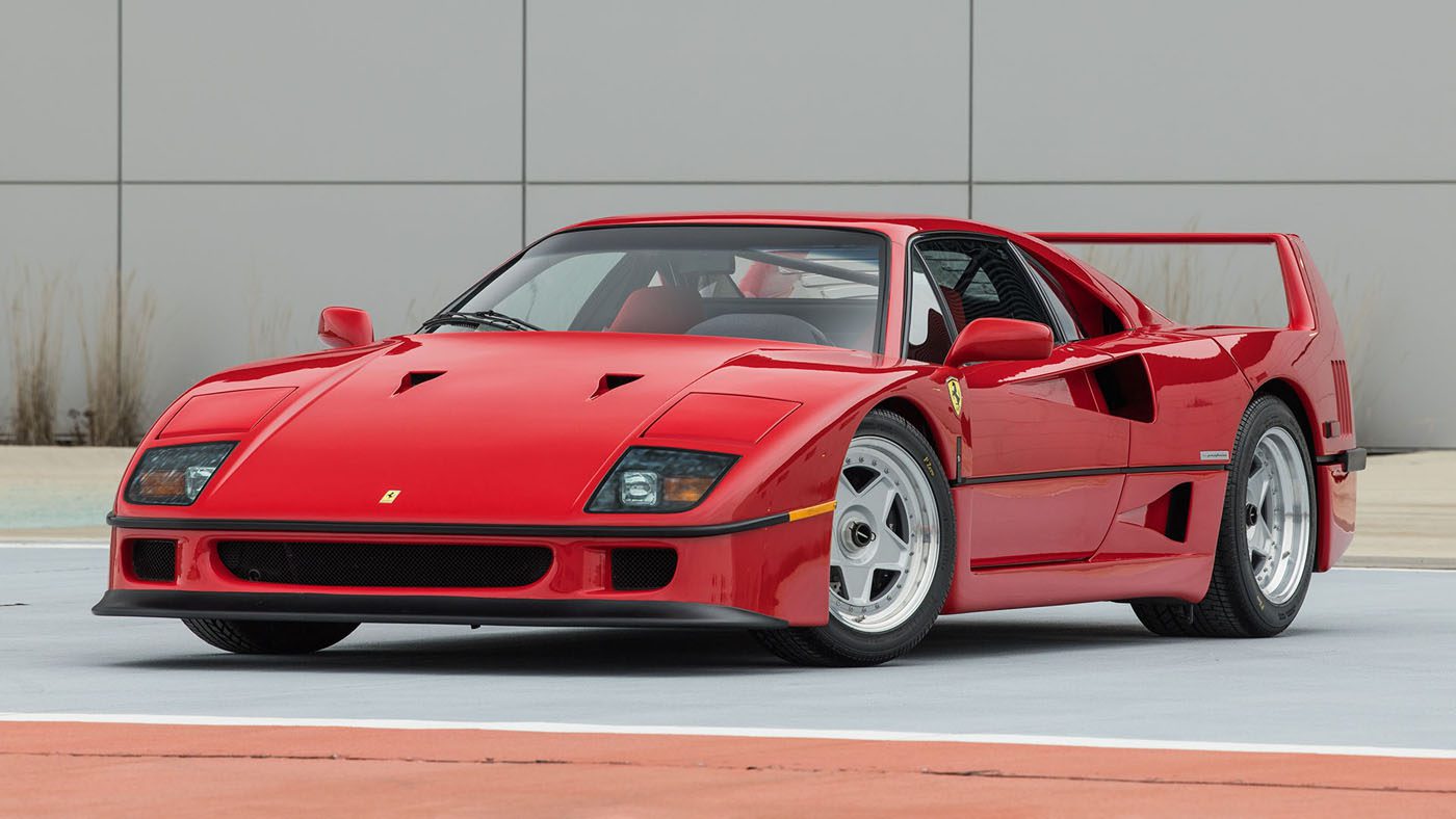 A sleek Ferrari F40 sports car is parked on the tiled surface, showcasing its large rear spoiler. This exquisite design could easily find itself at home among the elite offerings of Broad Arrow Auctions at Amelia Island.