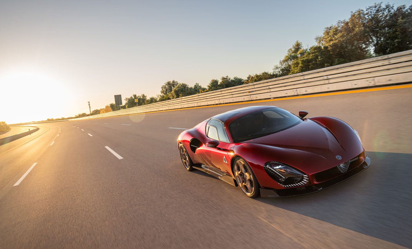 As sunrise paints the horizon, an Alfa Romeo 33 Stradale speeds down the highway, its silhouette slicing through the morning glow while trees blur in the background.