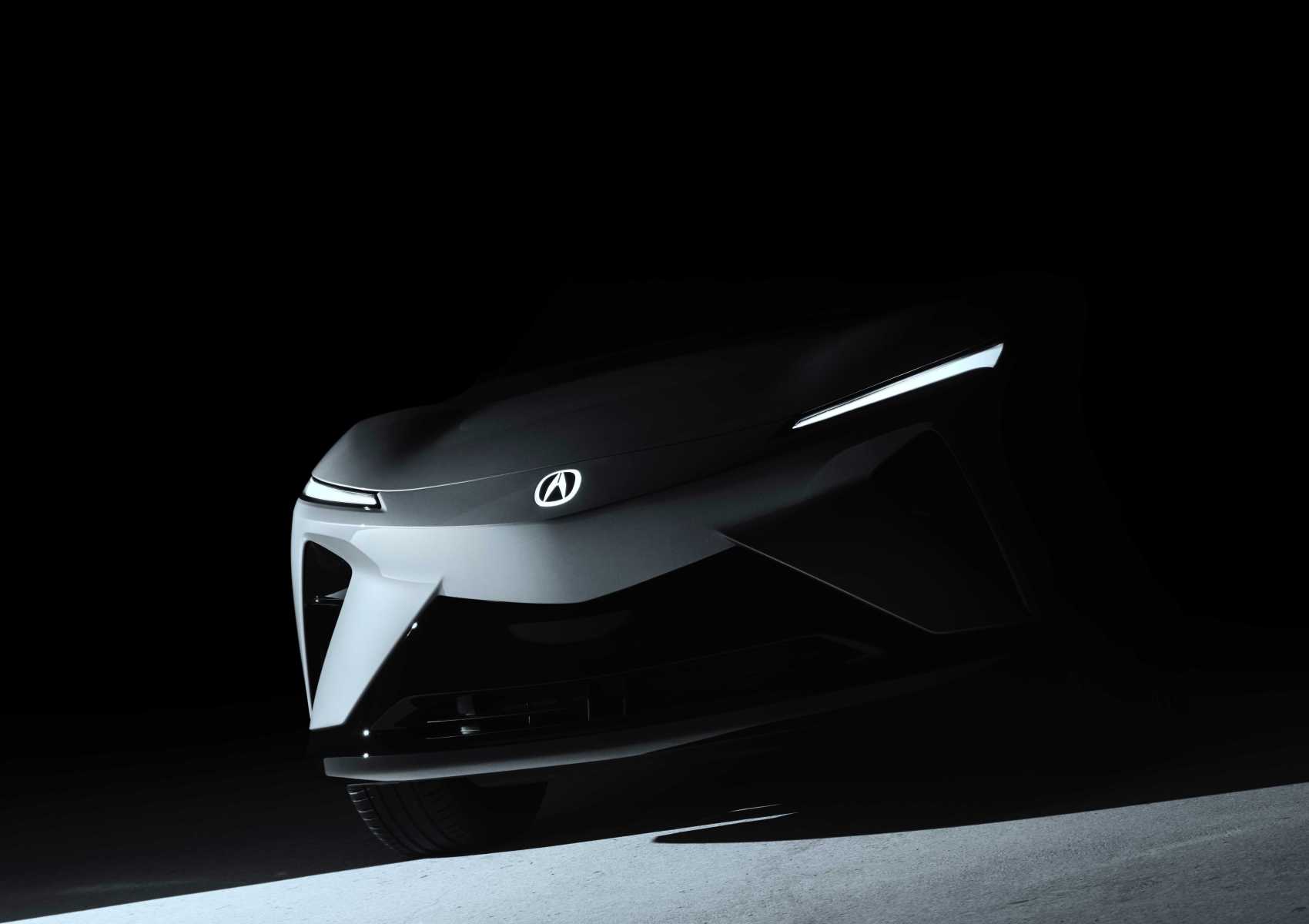 A dark, shadowed view of the front end of an Acura RSX Prototype EV Set for Global Debut at Monterey, featuring illuminated slim headlights and the iconic Acura logo.