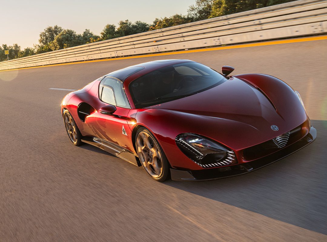 An Alfa Romeo 33 Stradale speeds along the track, as Valtteri Bottas expertly navigates each curve, with a barrier and trees in the background.