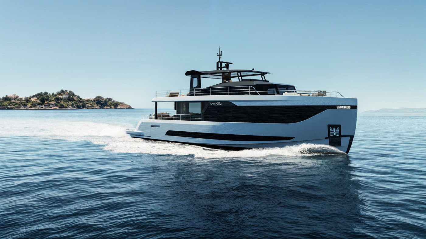 An elegant Arcadia Yachts A80new glides across calm blue water, its modern white and black design reflecting a commitment to sustainability, with a distant island visible on the left under a clear sky.