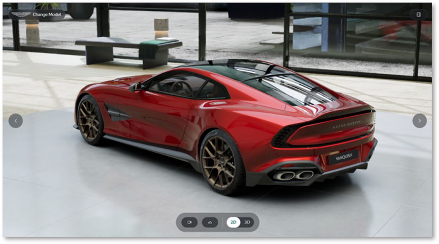 A red Aston Martin sports car with bronze alloy wheels is parked indoors on a concrete floor near large windows, capturing the refined look you can create with the Aston Martin online configurator.
