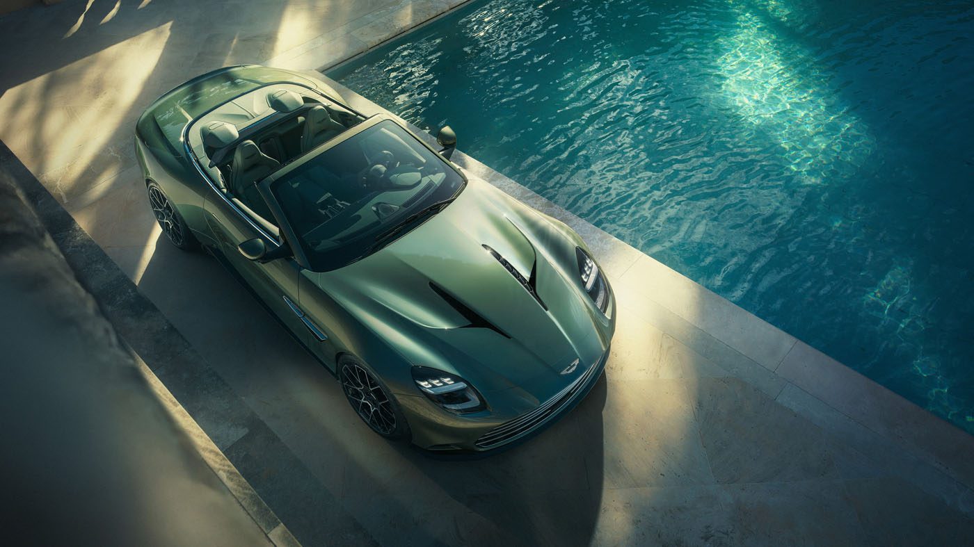 A sleek Aston Martin Vanquish, the fastest front-engined convertible, sits elegantly beside a pool, with the sun casting enticing shadows over its luxurious curves.