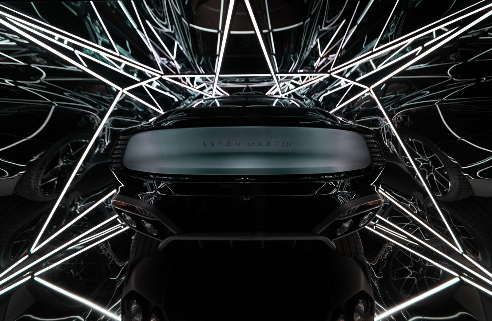 An Aston Martin Vanquish Supercar stands proudly, its sleek design enhanced by a vibrant light sculpture. The intricate pattern of white LED lights casts mesmerizing reflections and geometric shapes around the iconic vehicle's silhouette.