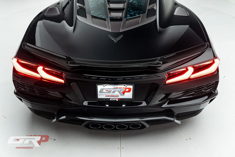 Rear view of a black C8 Corvette sports car with angular taillights illuminated, quad exhaust pipes, and a GRP Performance license plate in a white studio setting, showcasing the bold design of mid-engine American muscle.