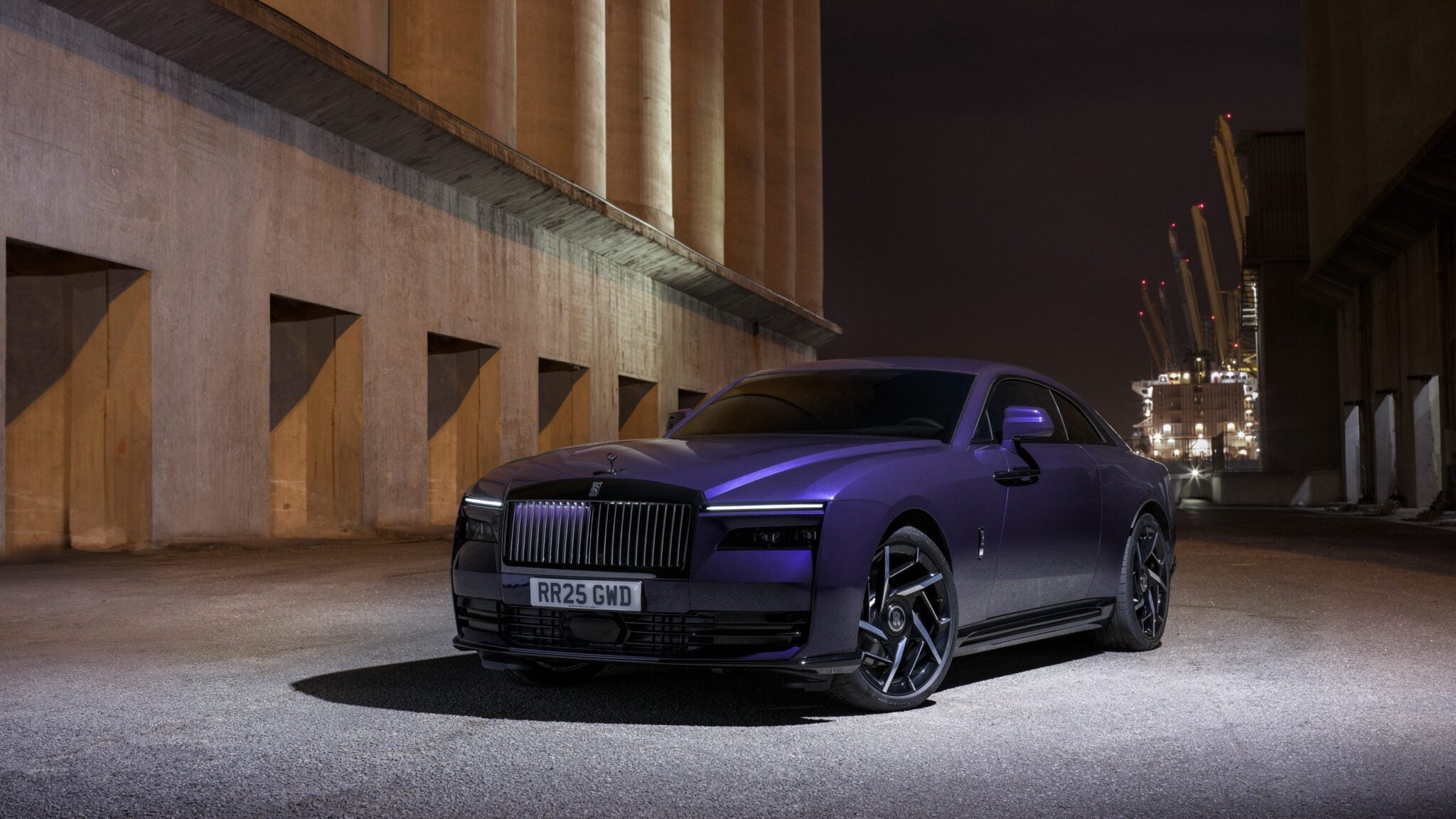 A purple luxury car is parked in a dimly lit industrial area at night.