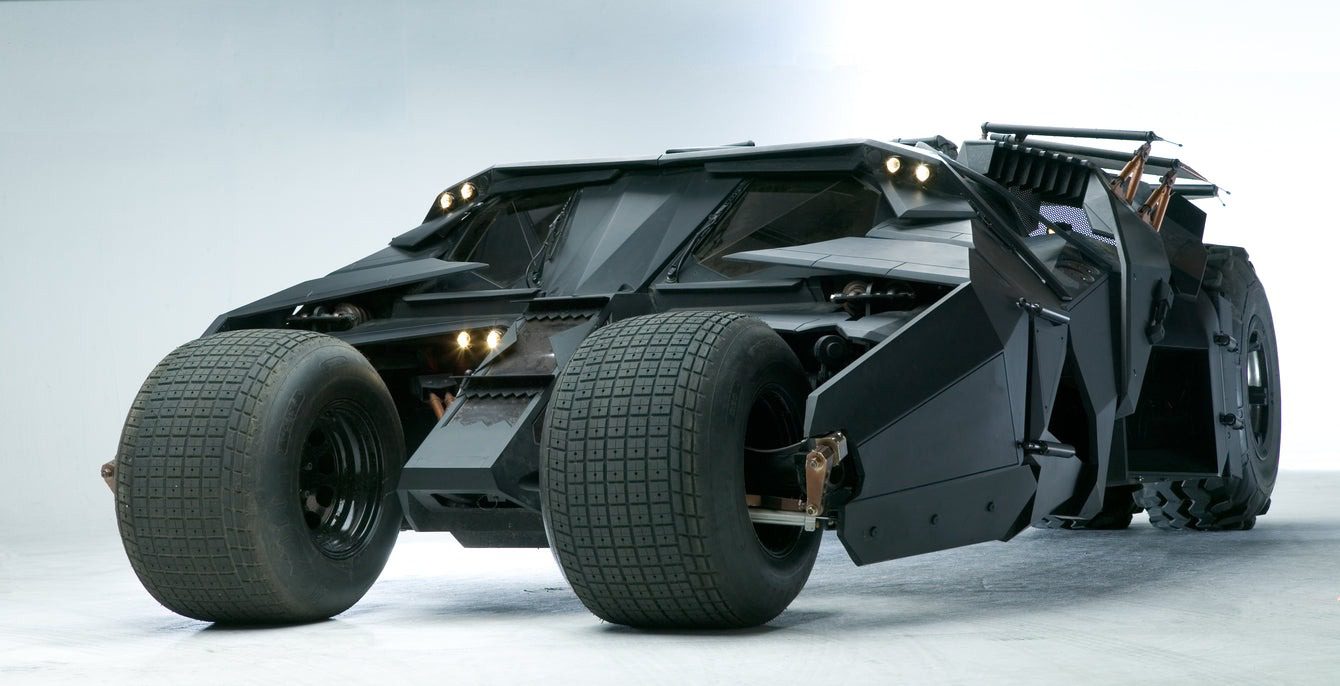 Futuristic black Batmobile armored vehicle with large tires, angular design, and multiple headlights, set against a plain background.