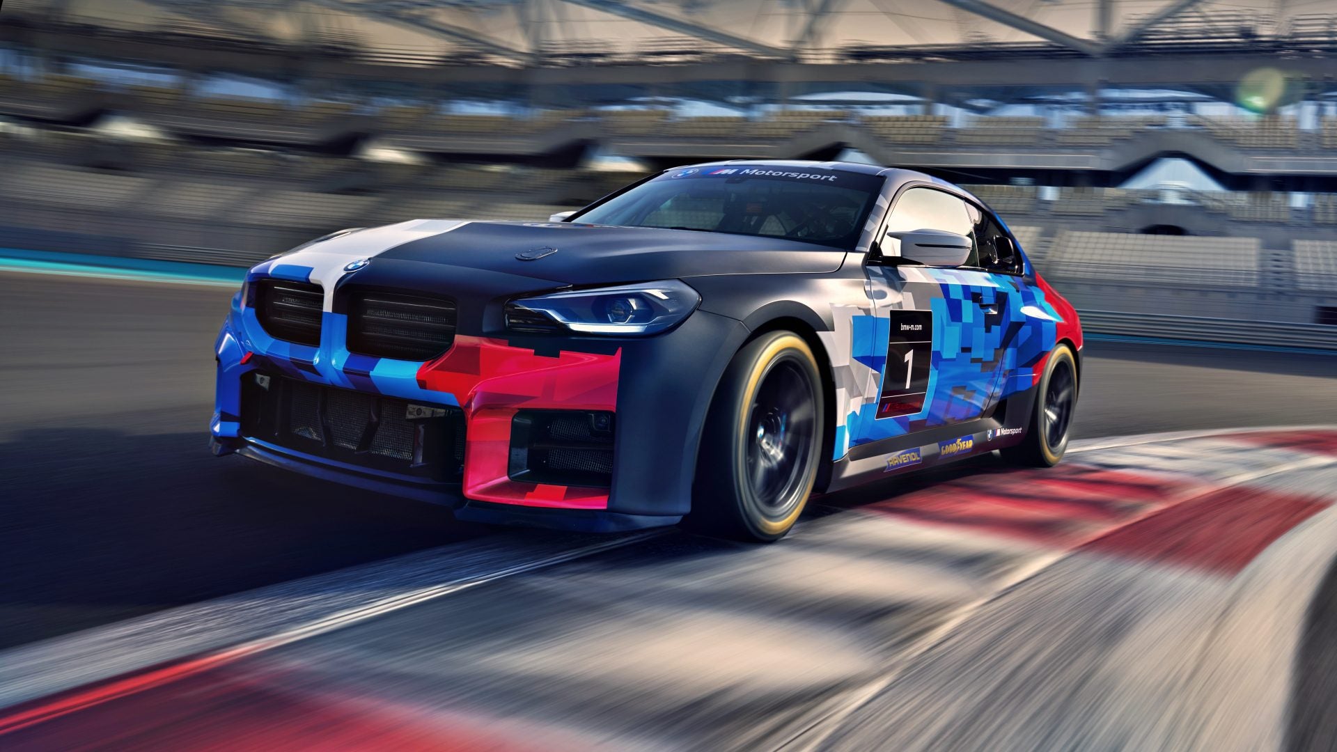 A BMW M2 Racing car with geometric blue and red graphics speeds along a racetrack, approaching a corner as the blurred stands rush by in the background.
