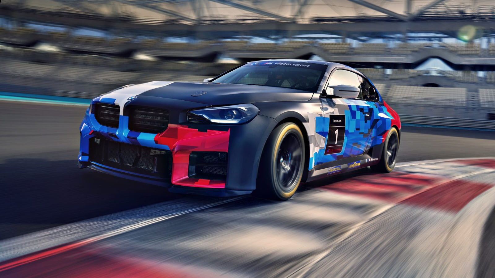 A BMW M2 Racing car with geometric blue and red graphics speeds along a racetrack, approaching a corner as the blurred stands rush by in the background.