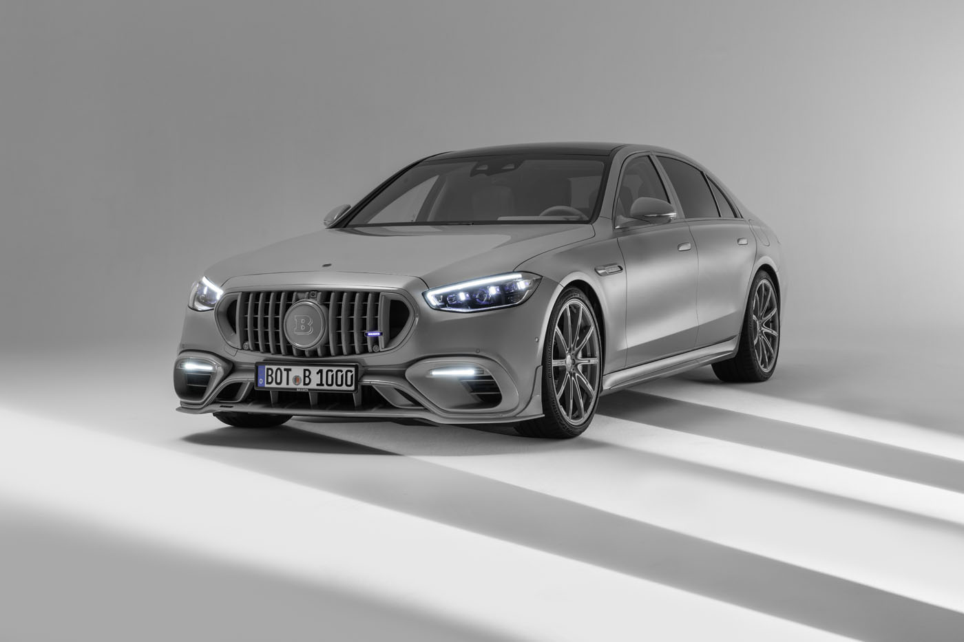 A BRABUS 1000 silver luxury sedan with bichromatic elegance, LED headlights, and a distinctive grille is parked in a well-lit studio setting.
