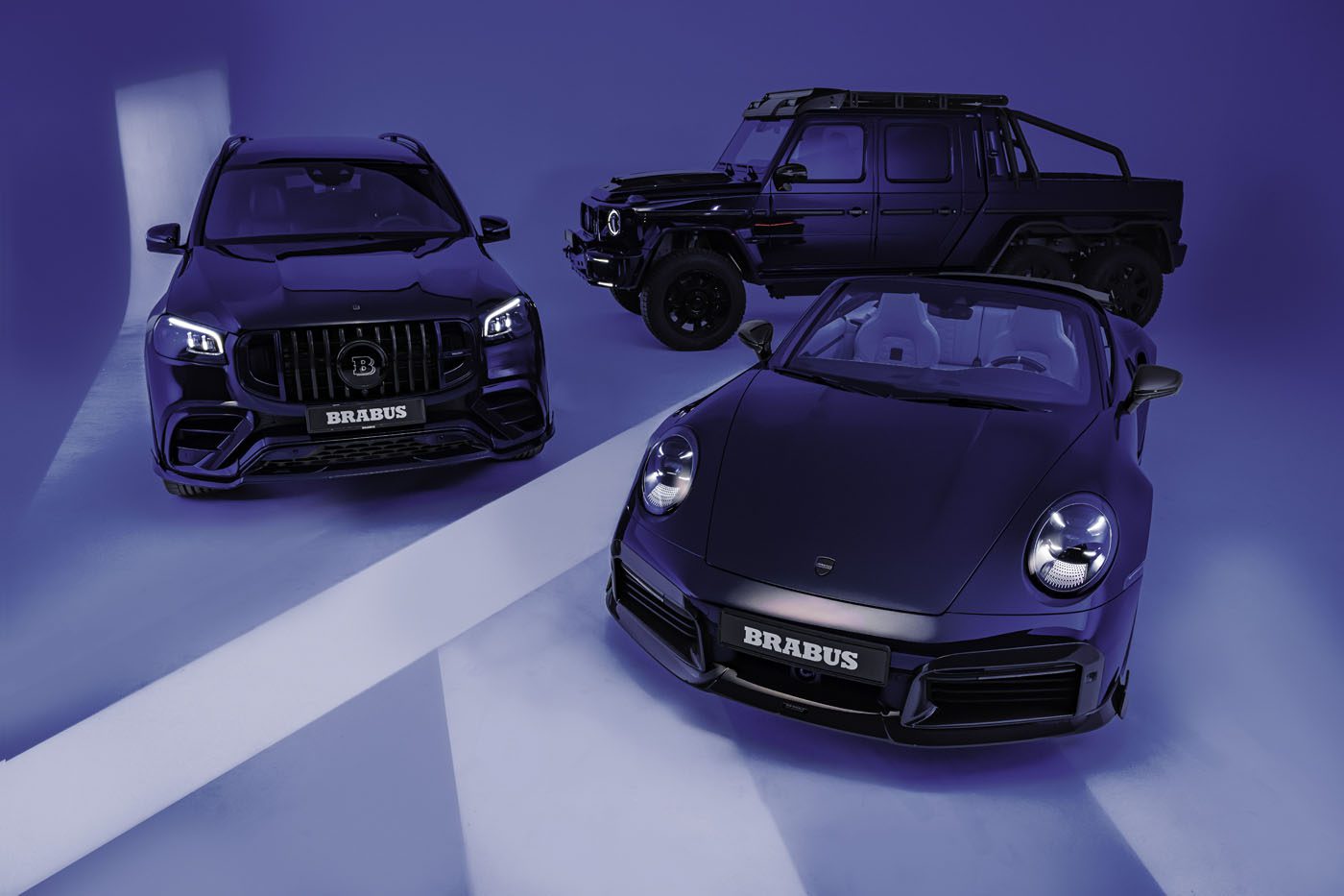 In the Deep Blue Series showroom, three luxury cars—a BRABUS SUV, a BRABUS off-road vehicle, and a convertible sports car—stand majestically in dark hues against a sleek, blue-lit backdrop.