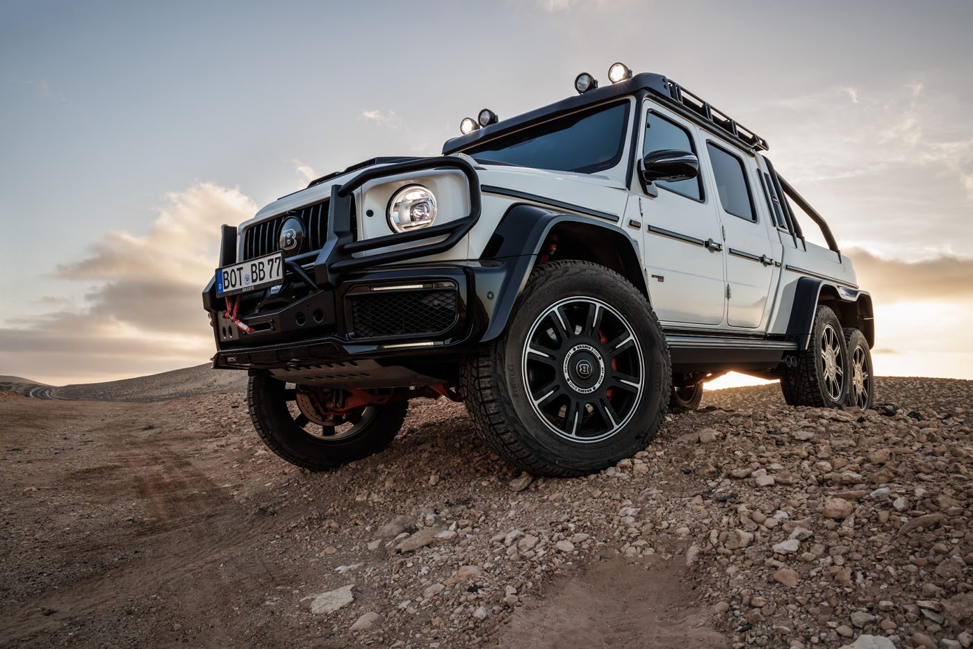 A BRABUS XLP 800 6x6 ADVENTURE Mercedes-Benz G-Class off-road vehicle is parked on rocky terrain at sunset.