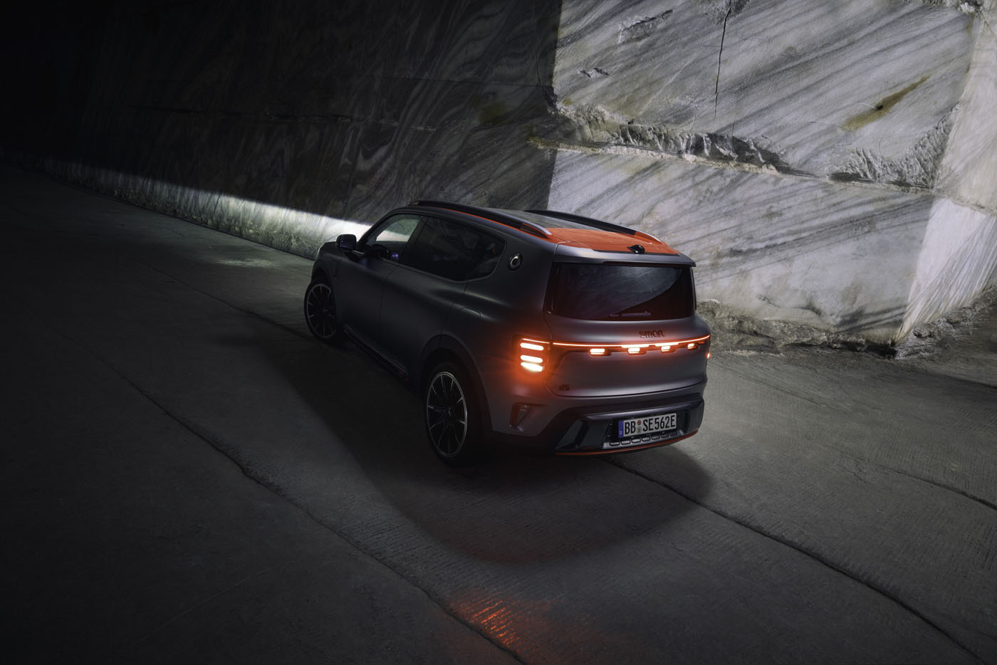 A dark-colored SUV, boasting an impressive 637HP by BRABUS, cruises with illuminated taillights through a dimly lit tunnel beside a stone wall.