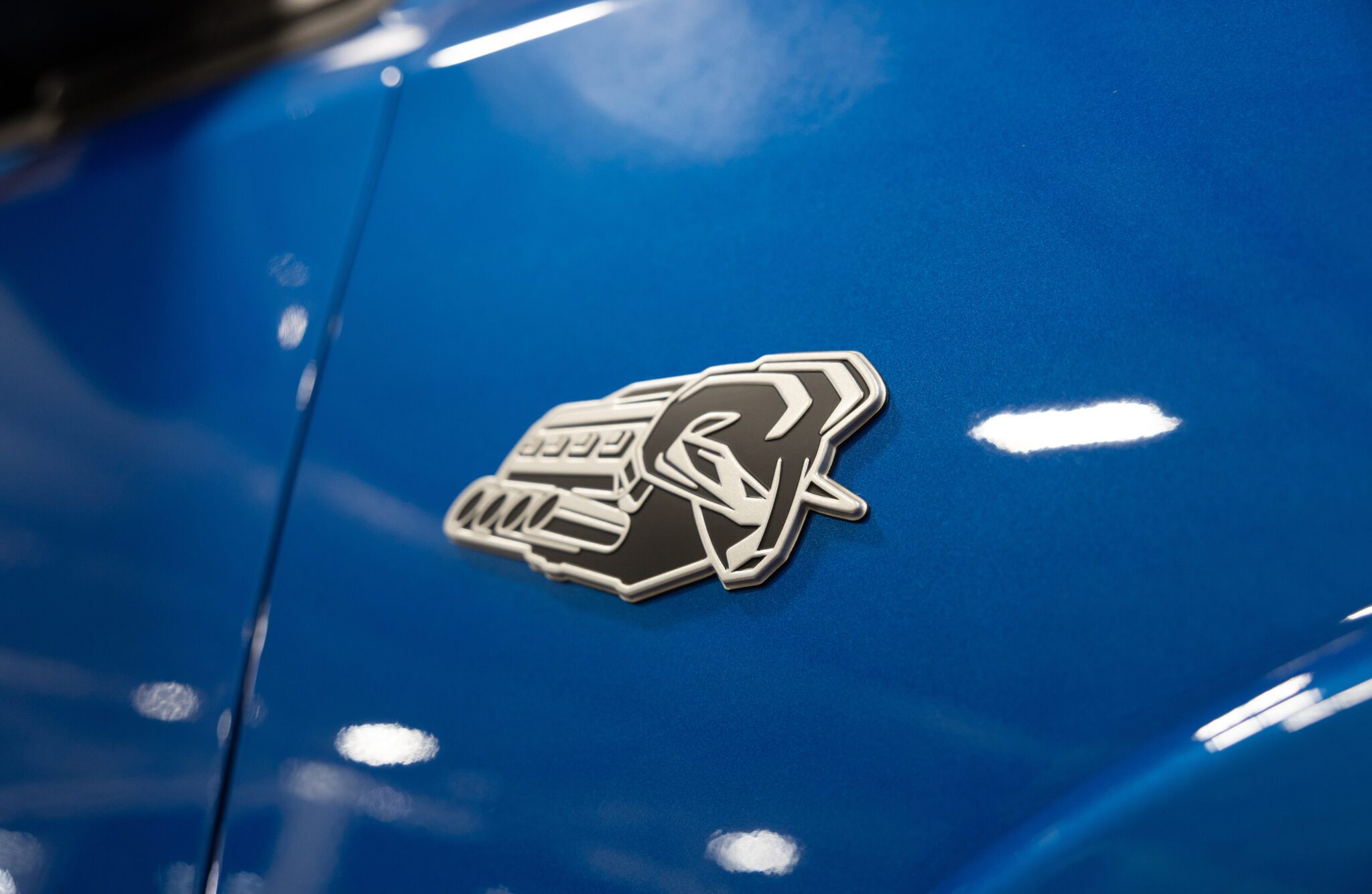 A close-up of a black and silver snake emblem on the side of a blue vehicle, celebrating the return of power as The HEMI Is Back: First 2026 Ram 1500 V8s Roll Off the Line.