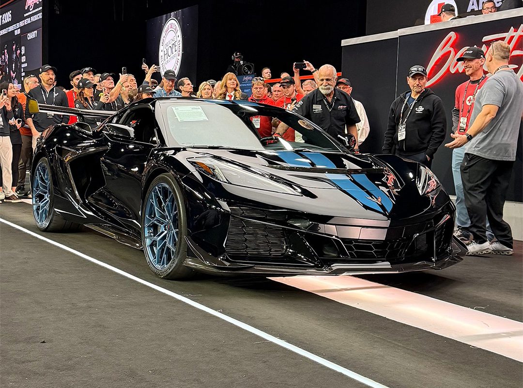 A sleek black Chevrolet Corvette ZR1 is displayed on a stage at Barrett-Jackson in Scottsdale, surrounded by people taking photos and admiring it.