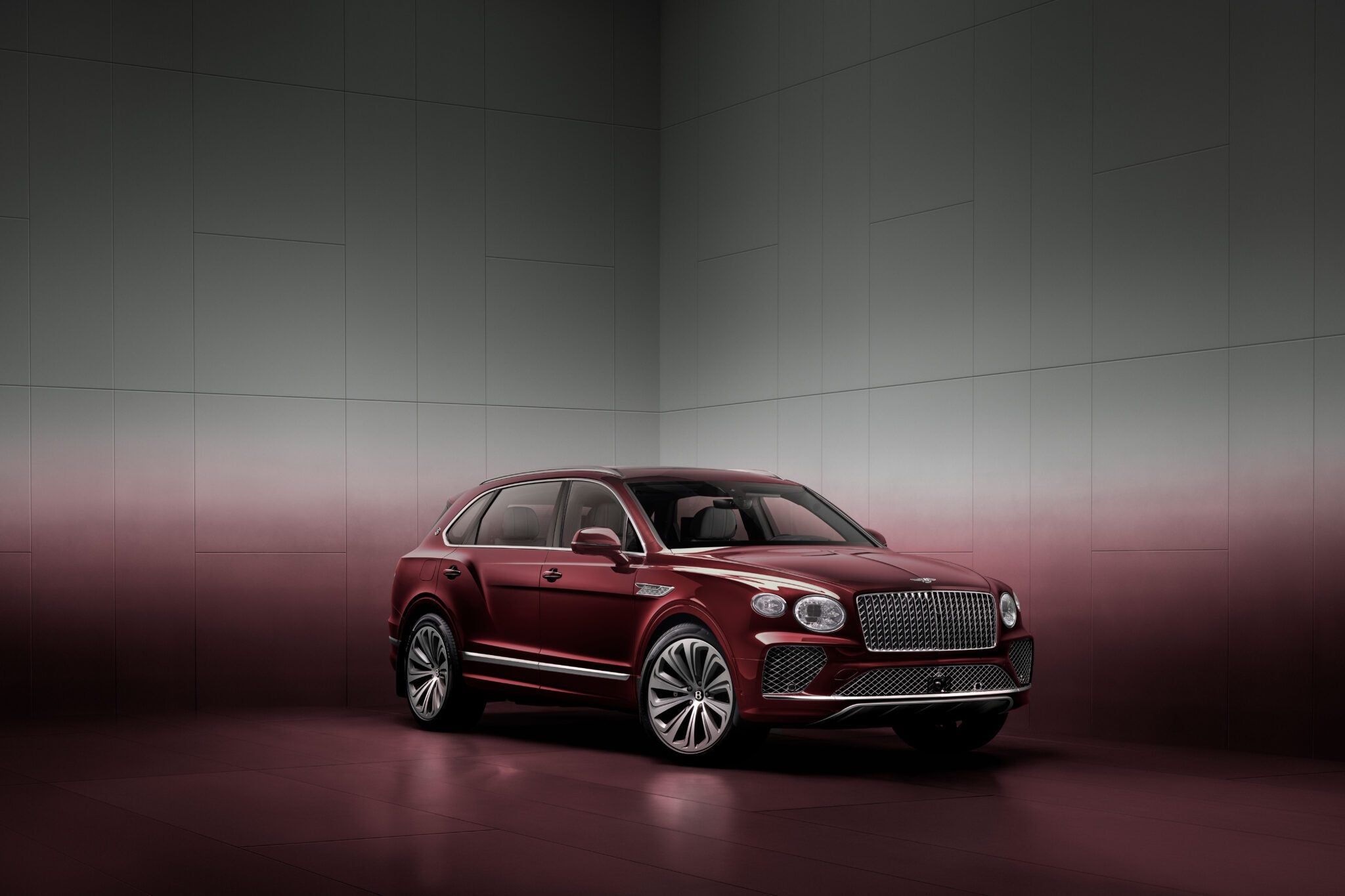 A maroon luxury SUV is parked in a minimalist, gradient-colored room with a reflective floor.