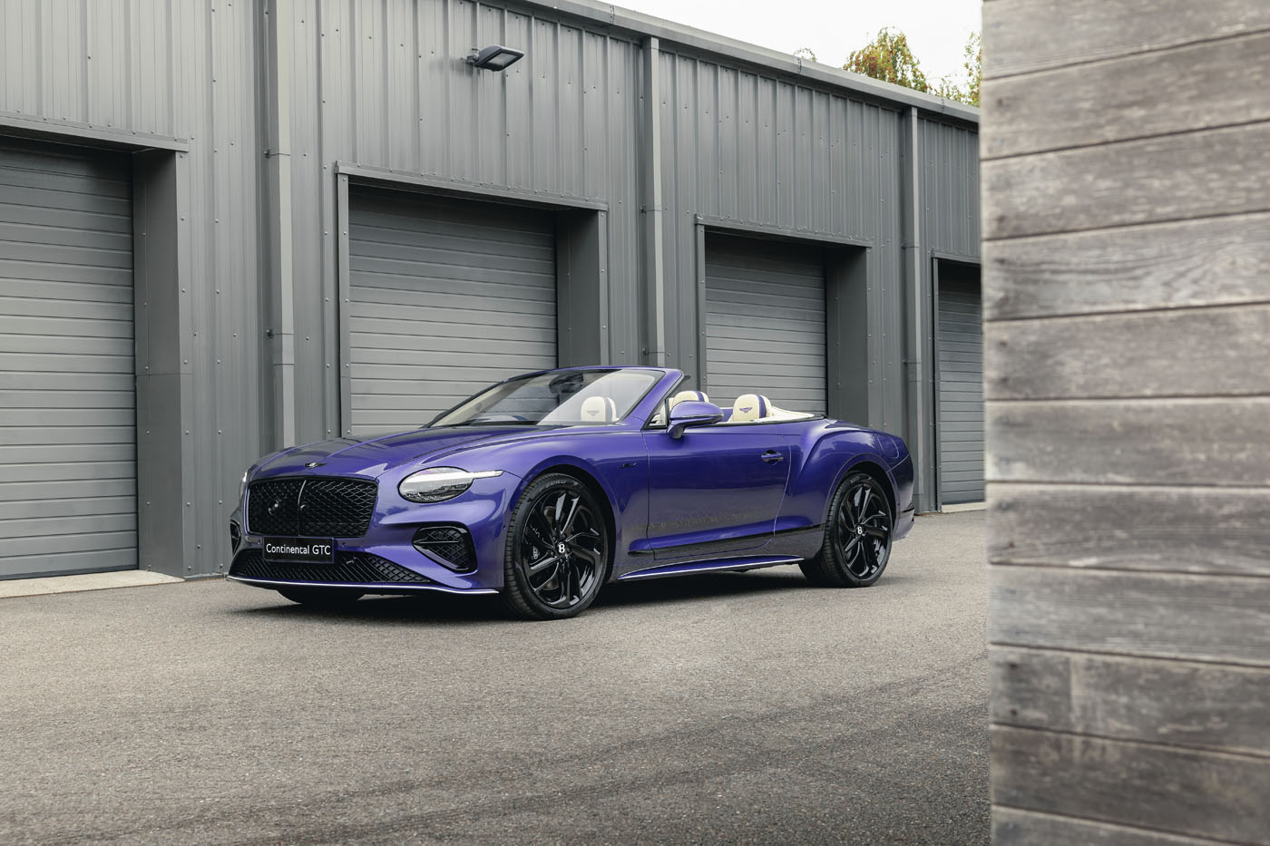 A bespoke Bentley Continental GTC in the striking Violette color is parked in front of a row of gray garage doors on a paved surface.