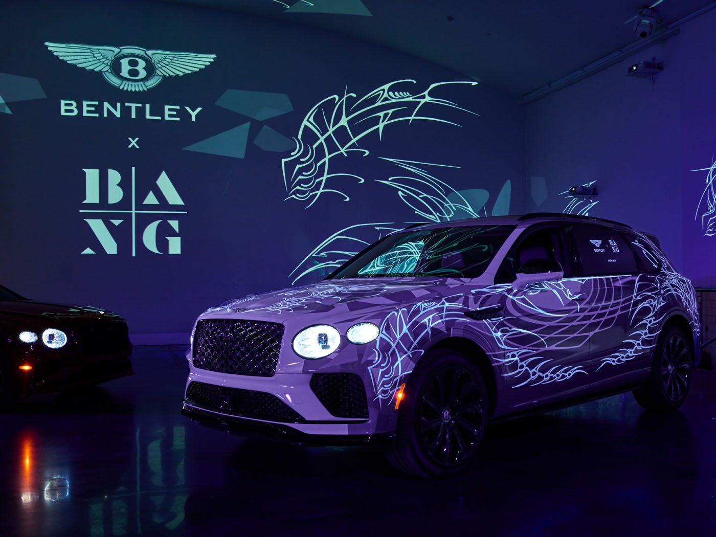 In a dimly lit showroom, a white Bentley Bentayga with color-changing illuminated patterns takes center stage, surrounded by branding and abstract designs on the walls.