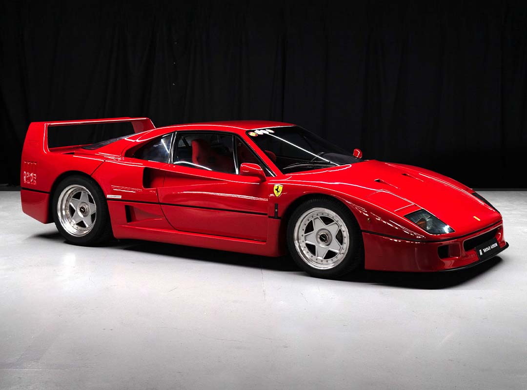 A red Ferrari F40, one of the ultimate '90s Icons, is parked indoors on a light floor with a black background.