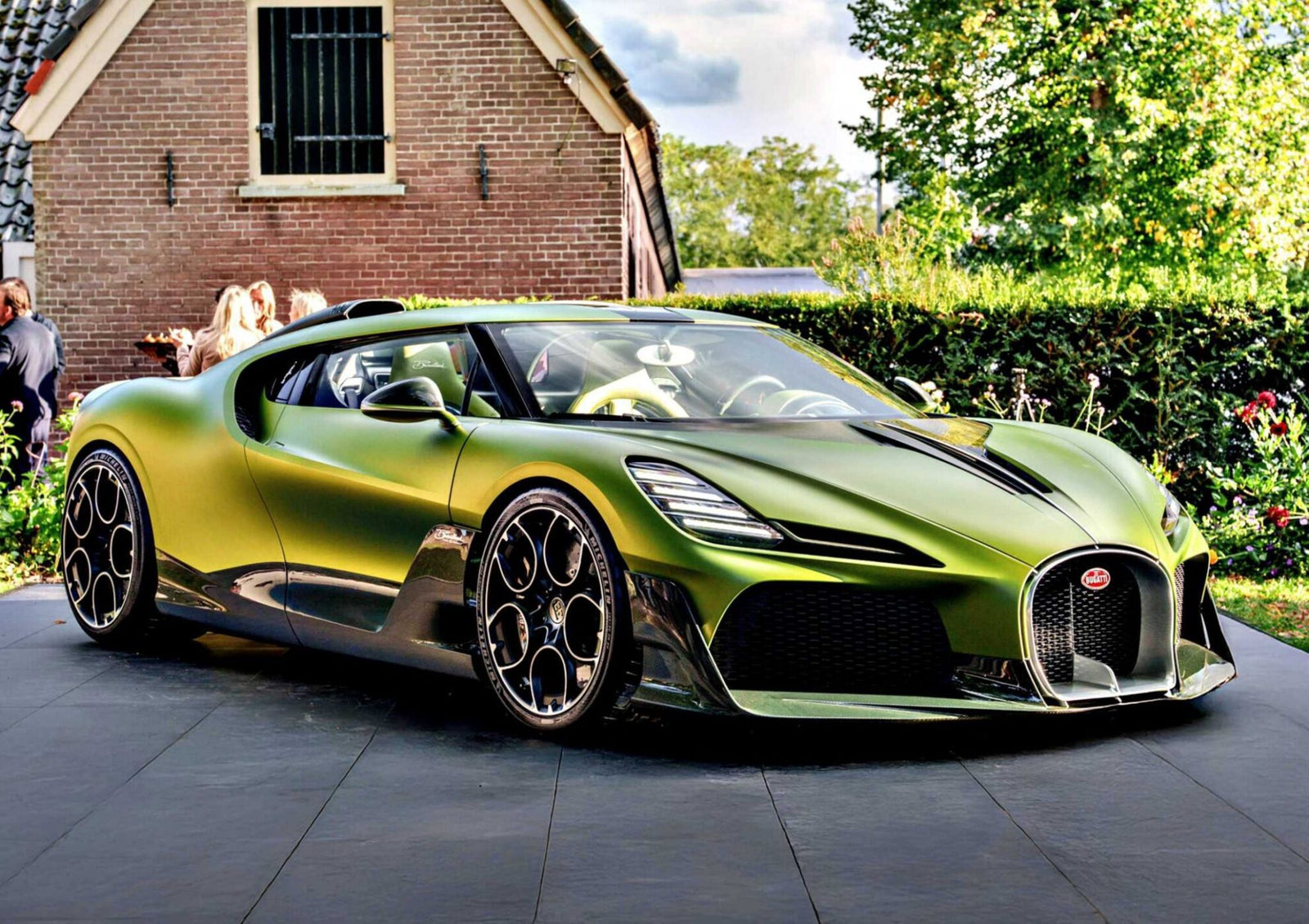 A green 1-of-1 Bugatti Brouillard is parked on a paved driveway in front of a brick house with lush greenery—making its stunning European debut at Wheels Mariënwaerdt.