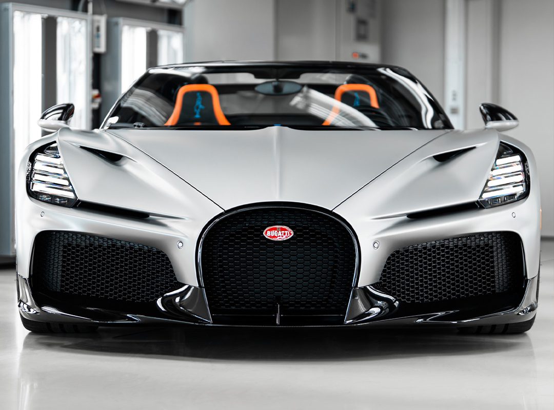 Front view of a silver $5M Bugatti Mistral with black grille and orange-accented seats, parked indoors—captured by Matt Argent.