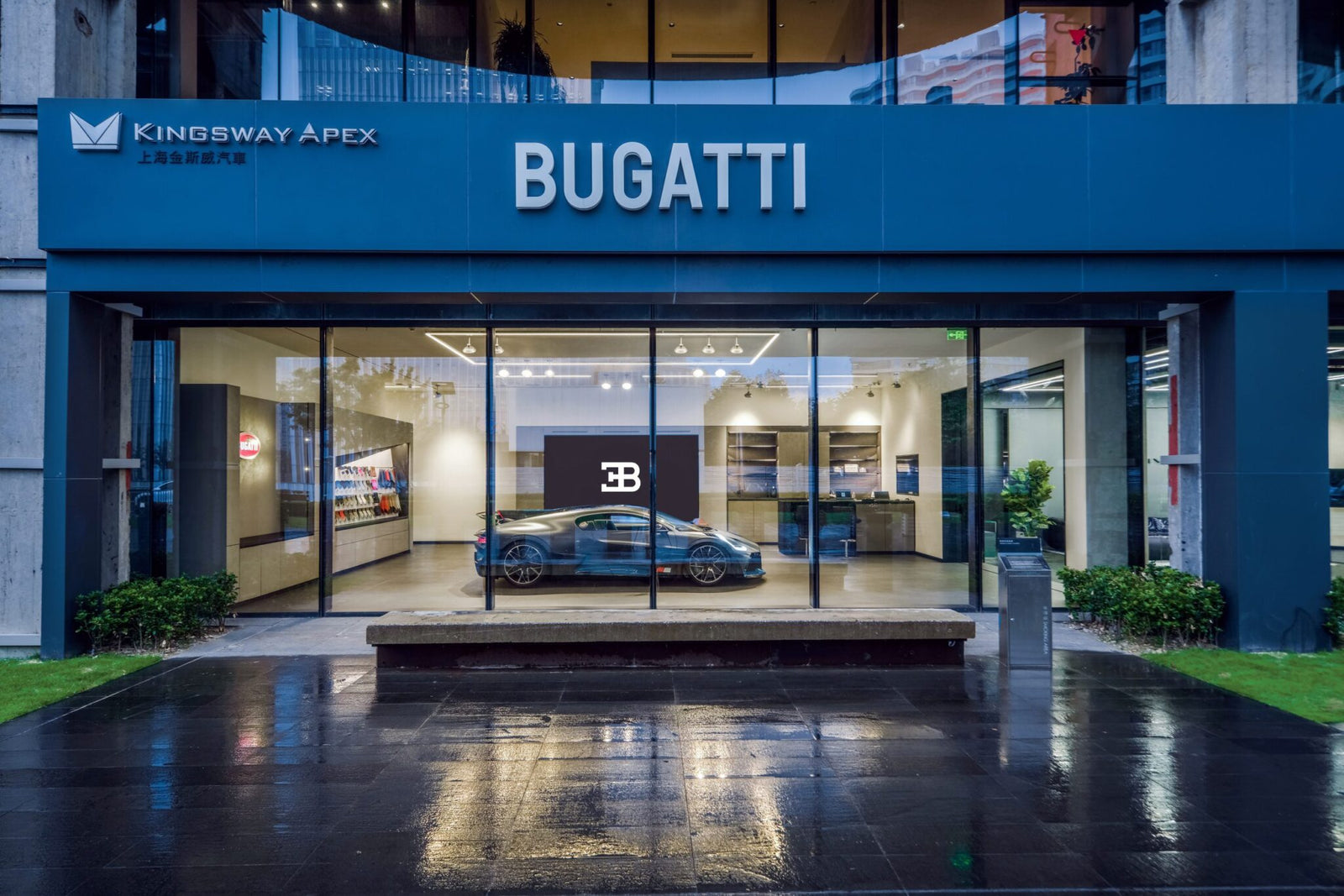Bugatti dealership exterior with large glass windows displaying a Bugatti car inside; "BUGATTI" sign above entrance and "Kingsway Apex" sign on upper left, representing a premier Shanghai showroom in Mainland China.