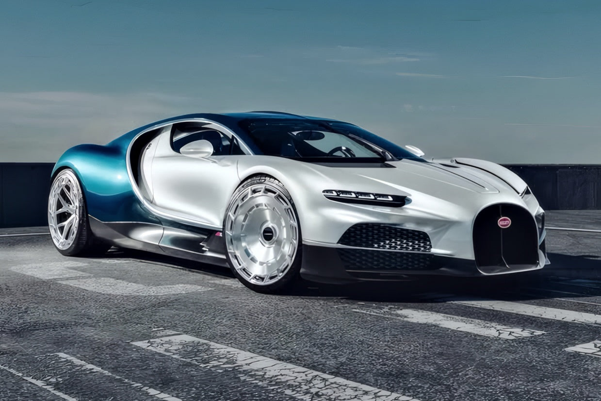 A silver and blue Bugatti V16 luxury sports car fitted with sleek Vossen wheels is parked on a rooftop with a clear sky in the background.