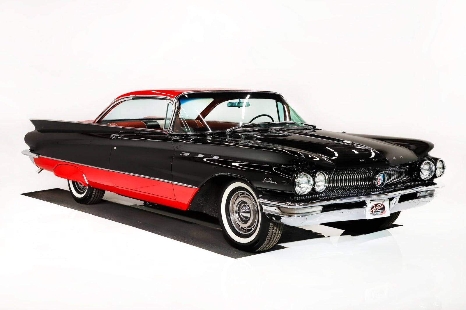 A vintage black and red two-door car with whitewall tires is displayed in a white studio setting, capturing the timeless allure of a Hollywood Classic.