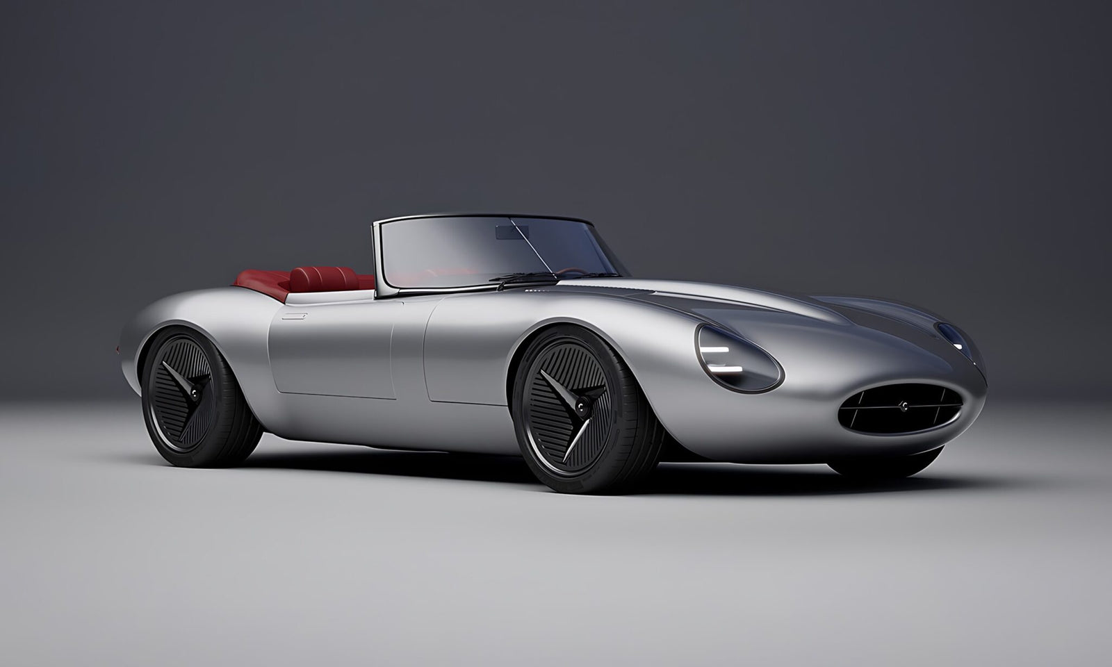 A silver convertible sports car with a sleek, aerodynamic design and red interior, shown in a studio setting—reminiscent of how former Jaguar designer Ian Callum reimagines a modern-day E-Type.
