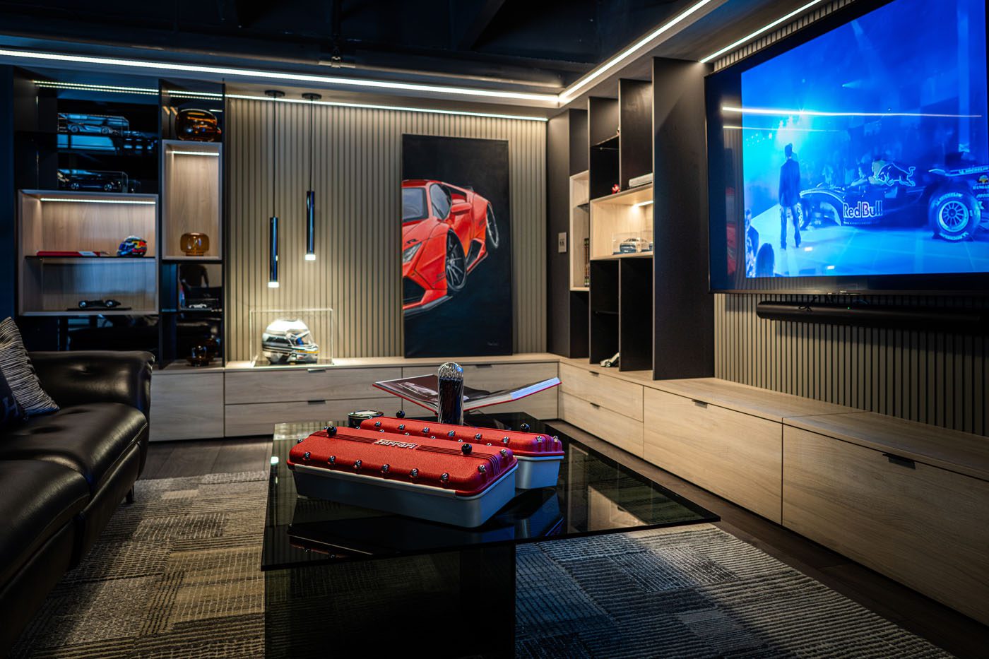 Modern entertainment room with a large wall-mounted TV showing a racecar, a black leather sofa, car-themed decor, and a glass coffee table displaying automotive items—perfect for Palm Beach luxury car collectors or CollectionSuites enthusiasts.