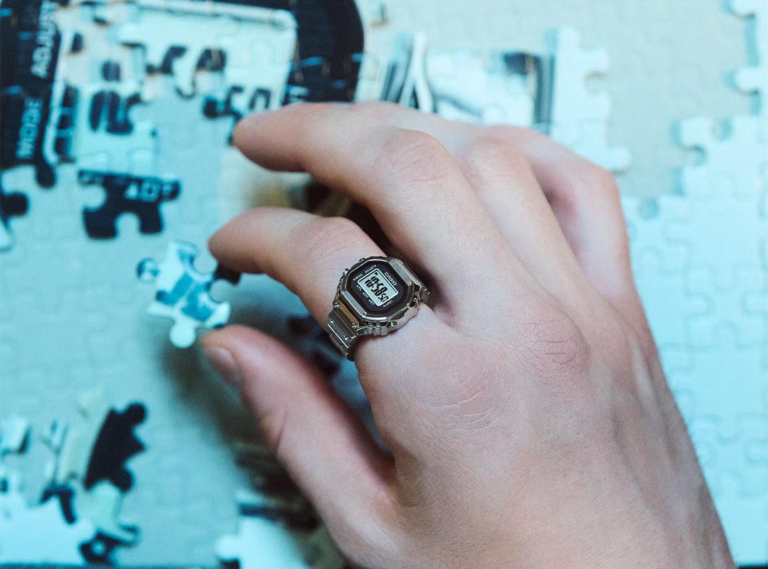 A hand sporting a sleek CRW-001 digital watch is placing a puzzle piece onto a partially completed puzzle.