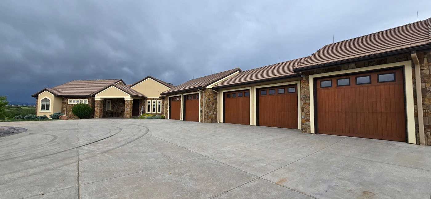 Large single-story house with a tan exterior, stone accents, and four wooden garage doors sits on a wide concrete driveway under a cloudy sky—offering unique opportunities through CWS Marketing Group.